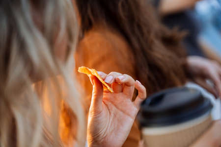 A girl eats snacks outside drinking coffee, a woman's hand holds a piece of cookies, dried mango is clamped in the girl's fingers, breakfast outside, fast food. high quality photoの写真素材