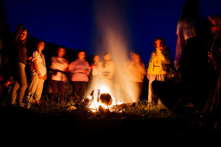 People in a blurred background dance at night by the fire, a fire show, dancing with a tambourine, shamanic rituals in nature, evening dances, a large fire of firewood. high quality photoの写真素材
