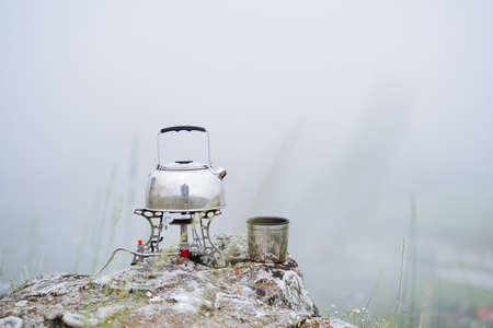 A small kettle stands on a gas burner in the mountains, boil water on a tourist burner, drink tea on...