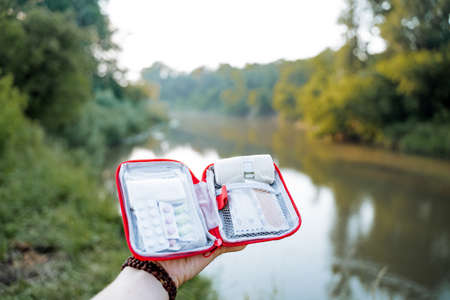 A tourist first-aid kit lies in a person's hand against the background of nature, an open first aid kit, a set of medicines and tablets, the insides of a medic's bag. high quality photoの写真素材