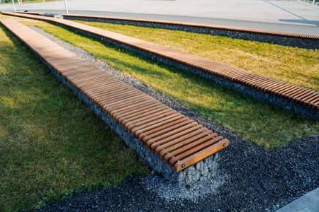 Street landscape of the city park, wooden benches made of boards, lawn for relaxing in the shade of...