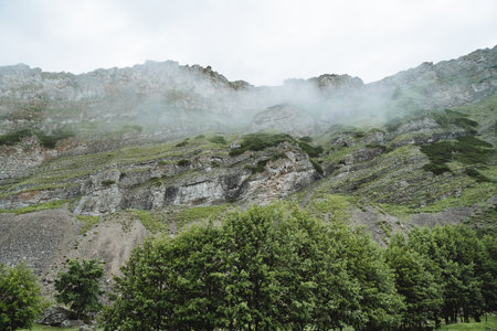 The stone wall of the mountain gorge, the canyon view from below, a high mountain in the fog, rocky...