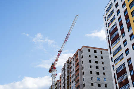 A construction crane against the background of a multi-storey building, a construction site, the construction of a residential building, a long boom of a crane. high quality photoの写真素材