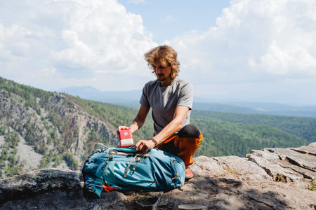 Take the first aid kit out of the backpack, the guy puts a first aid kit in the backpack, a tourist in the mountains collects equipment, a man on top of a mountain. high quality photoの写真素材