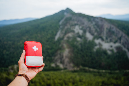 demonstration of a first aid kit on a hike, a hand holding a first aid kit, a red bag with medicines against the background of mountains, equipment on a hike. high quality photoの写真素材