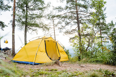 A yellow tent stands in the forest high in the mountains, tourist camping, a summer day in nature, a vacation in the forest, an open entrance. high quality photoの写真素材