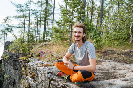 The guy smiles sitting on a rock in the mountains, hiking, outdoor recreation, sitting posture, a kind man. high quality photoの写真素材