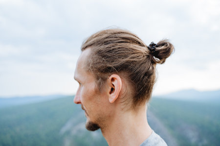 Hairstyle on the head of a man, sloppily collected hair, a view from behind a man's hairstyle, a pigtail on his head, a bearded hipster in the mountains. high quality photoの写真素材