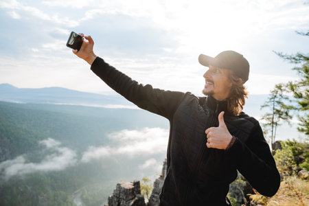 Selfie against the background of nature, a guy takes pictures of himself on his phone, A photo for memory, a tourist in the mountains, a smartphone in his hand likes on the cameraの写真素材