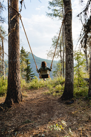 The swing is tied to a tree, the view behind the girl swaying on the swing, the attraction with the rope, soaring in the air. high quality photoの写真素材
