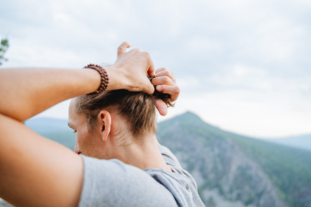 The guy collects the hair on his head with his hands, the youth hairstyle of a hipster, the view from behind a man tying his hair in a bun. high quality photoの写真素材