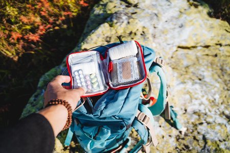 The hand holds a first aid kit, a set of first aid medicines, a tactical first-aid kit lies in a backpack, an elastic bandage, tablets in a set, an alarm bag.の写真素材