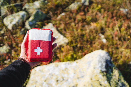 First aid kit, hand holding a first aid kit, a red bag with a white cross, an ambulance in the forest, camping equipment, a first-aid kit.の写真素材