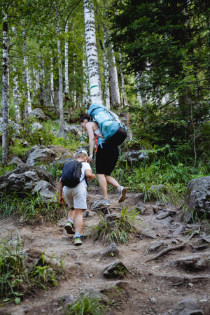 Family trip to the mountains, mother and son climb the trail in the mountainous area, children's tourism, trekking with backpacks in the forest, outdoor holidays. high quality photoの写真素材