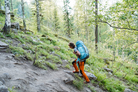 A person climbs uphill on a trail with a large backpack on sleep, hiking alone, mountain climbing, hiking, forest walk. High quality photoの写真素材