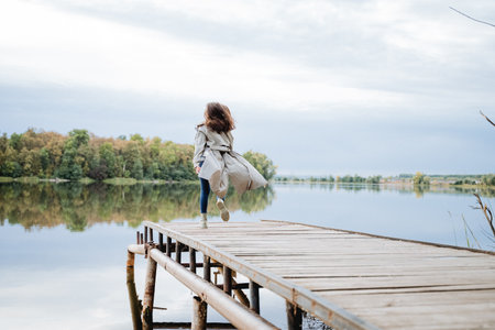 A girl in a raincoat runs across a bridge into a river, a man wants to jump in clothes into the water, a pier on a lake, a woman walks in a park near a reservoir. High quality photoの写真素材