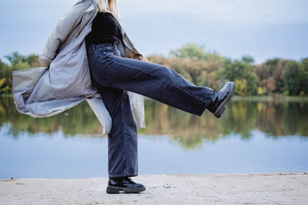 Girl taking a wide step forward, swinging her leg up, autumn clothes for walking, girl in a raincoat, wide jeans, teenager dancing.の写真素材