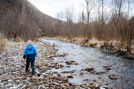 Child walking alone in nature, little boy walking along the river, children's play, rear view of schoolboy in the forest. Autumn weather, the first snow fell. High quality photoの写真素材
