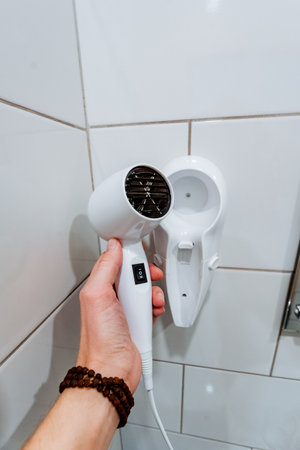 Hairdryer in the hands of a man in the bathroomの写真素材