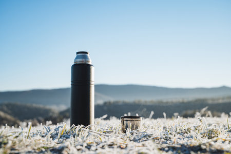Flask with mug on sky background, concept of tourist tableware for hot drinks, brewing tea outdoors in winter. Camping in the mountains. High quality photoの写真素材