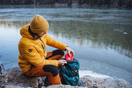 A guy on a hike sits on a rock and takes out a first aid kit from his backpack pocket, the concept of tourist trekking in the mountains, safety in nature. High quality photoの写真素材