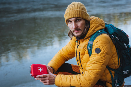 A young guy tourist holds a red first aid kit, a box with a white cross, survival in the forest, trekking in the mountains, first aid kit. High quality photoの写真素材