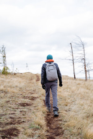 A guy with a backpack walks along a rocky path. He is dressed in comfortable hiking clothes and sneakers. His backpack is filled with everything you need for a comfortable trip in the mountainsの写真素材