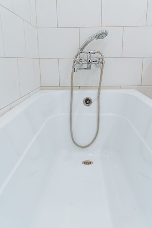 Bathroom with shower, shower head with hose in the bathtub, white plastic bathtub. High quality...
