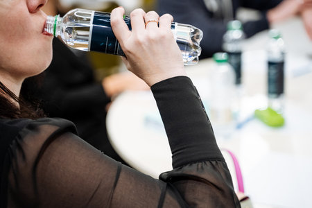 The process of drinking water, the girl drinks mineral water in large sips, quench her thirst, a bottle of mineral water. High quality photoの写真素材