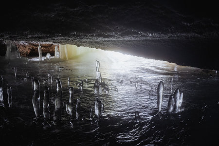 An underground cave covered with ice, ice stalagmites growing in the cave, frozen water underground, light at the end of the exit. High quality photoの写真素材