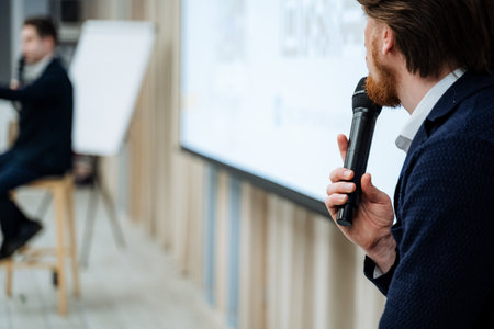Bearded man holding microphone in his hand, guy speaking in front of an audience, training at a business forum, speaking into a microphone. High quality photoの写真素材
