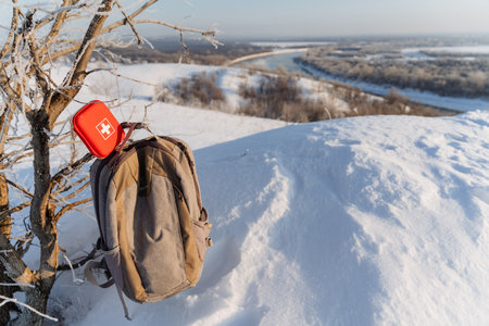 Hiking backpack hanging on a branch against the background of a winter forest, a red first aid kit...