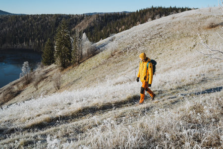 Man on mountain hike walking on road with backpack on back, trekking alone in winter in cold...