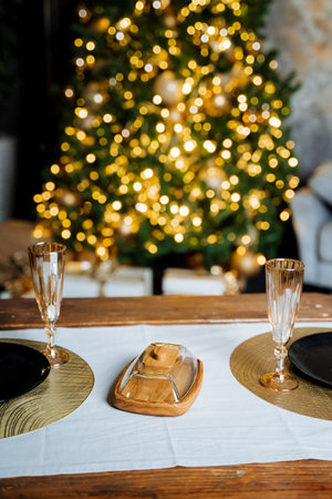 A New Year's table, lights on the Christmas tree, champagne glasses are on the table, a handmade butter can, a glass lid. High quality photoの写真素材