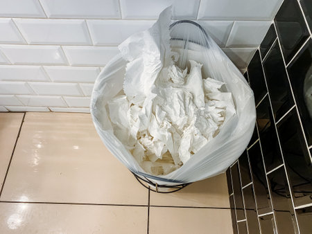In a bathroom, there is a trash can filled with tissues instead of the usual food, recipe,...