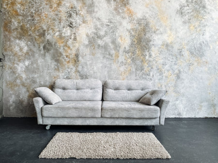 A gray studio couch made of wood is placed in front of a concrete wall in a living room, along with...