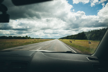 Countryside road with green field and blue sky. Car driving on highway through rural landscape with forest. Road trip concept. Perfect for driving and exploring natural scenery.の写真素材