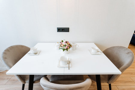 A white marble dining table with a beautiful bouquet of pink roses in a glass vase. Three...