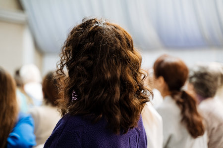 A woman with curly brown hair in a purple sweater attending a professional conference. She is...