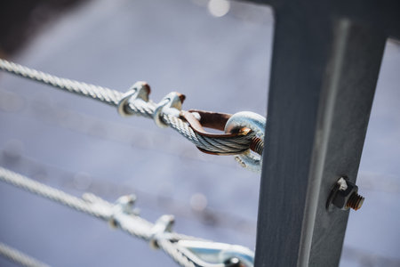 Close-up of metal cable railing with crimped loop fitting on stainless steel post. Gray cable, black post with bolt and nut for security on deck, balcony, or staircase.の写真素材