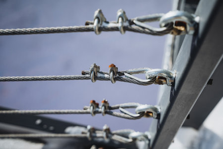 Close-up of intricate gray steel cables and shiny silver fasteners on a modern railing, showcasing an industrial design with strong metal elements and precise alignment in a horizontal pattern.の写真素材