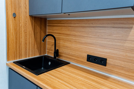 The kitchen features a black sink, wooden countertop, and modern tap. The cabinetry complements the wood, creating a harmonious look in the houseの写真素材