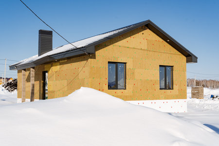 Construction of the house in winter, the house is in the snow, the facade is insulated with mineral wool, warm walls. High quality photoの写真素材