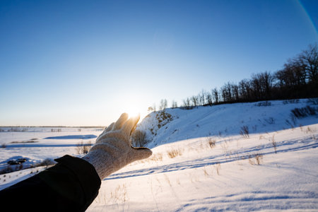 A gloved hand blocks the sunlight in winter, the glare of the setting sun shows through his fingers. Winter landscape, the beauty of Russia's nature. High quality photoの写真素材