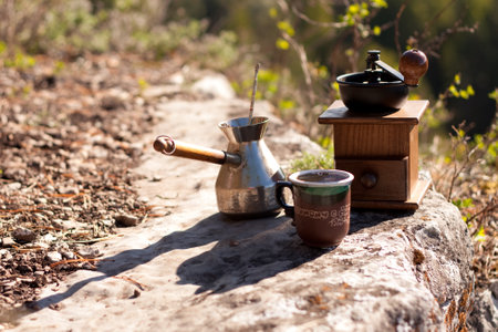 A coffee grinder and a cup of coffee are placed on a rock in a landscape surrounded by grass and water, adding a natural touch to the sceneの写真素材