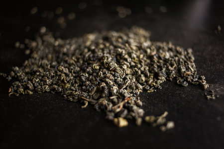 Macro photography of a pile of green tea leaves on a black surface resembles a plant growing in darkness, emerging from asphalt or rocklike soil. The dish captures the essence of cuisineの写真素材