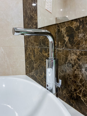 A bathroom fixture with a plumbing fitting, including a tap, sink, and marble wall, providing a stylish interior design touch.の写真素材