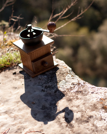 A quaint wooden coffee grinder rests on a rugged rock amidst a picturesque landscape of trees, grass, and soil, blending seamlessly with the natural materials of the surroundingsの写真素材