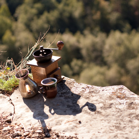 A toy coffee grinder sits on a bedrock next to two cups, overlooking the landscape. A rock, home to insects and arthropods, adds a touch of nature to the sceneの写真素材