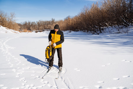 Man on skis standing on frozen river with backpack in hands, hiking in winter forest, solo trip. High quality photoの写真素材